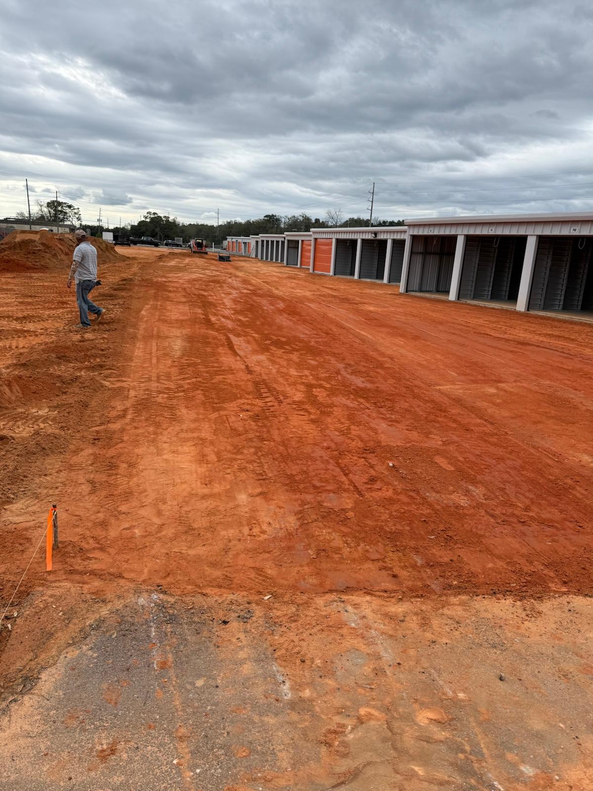 Freshly graded red clay lot alongside a new self-storage facility